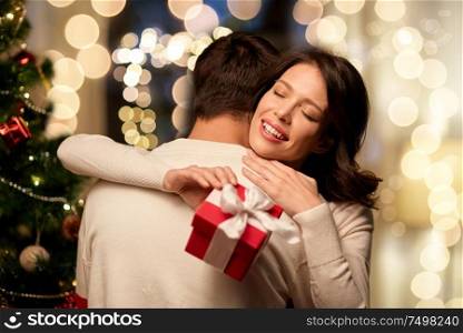 winter holidays and people concept - happy couple with christmas gift hugging at home. happy couple with christmas gift hugging at home