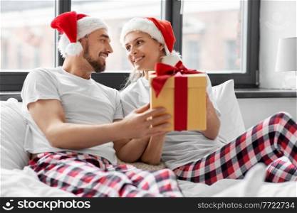 winter holidays and people concept - happy couple with christmas gift in bed at home. happy couple with christmas gift in bed at home