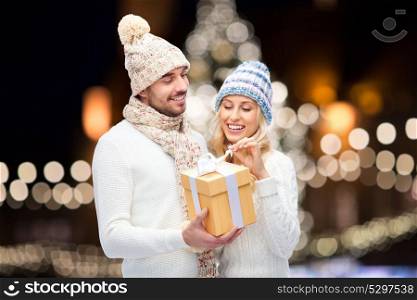 winter, holidays and people concept - happy couple with gift box over christmas tree lights background. happy couple with christmas gift over night lights