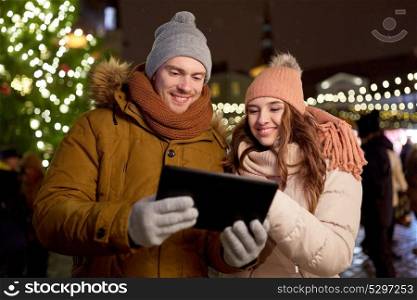 winter holidays and people concept - happy couple with tablet pc at christmas market in evening. happy couple with tablet pc at christmas market
