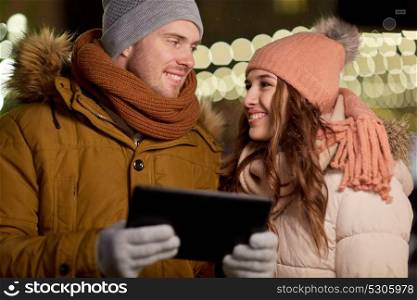 winter holidays and people concept - happy couple with tablet pc at christmas market in evening. happy couple with tablet pc at christmas market