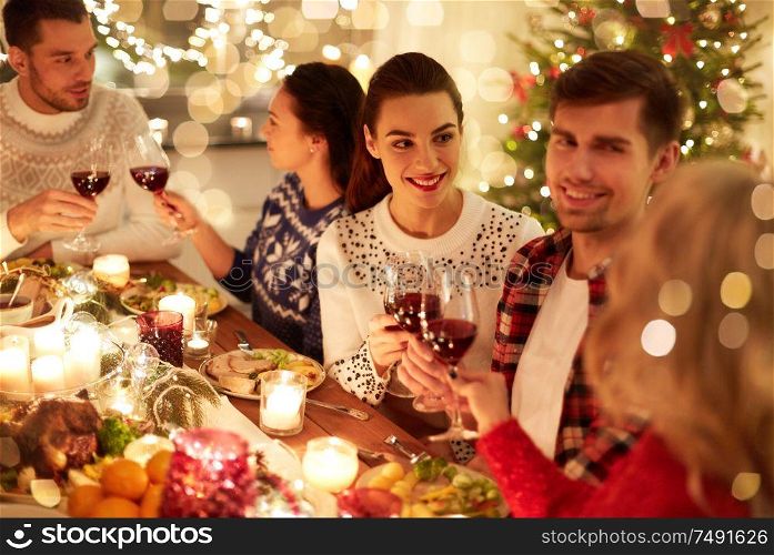 winter holidays and people concept - happy friends celebrating christmas at home feast and drinking red wine. happy friends celebrating christmas at home feast