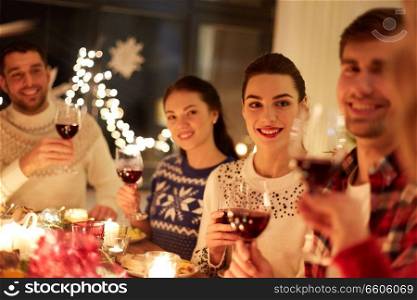 winter holidays and people concept - happy friends celebrating christmas at home and drinking red wine. happy friends celebrating christmas at home