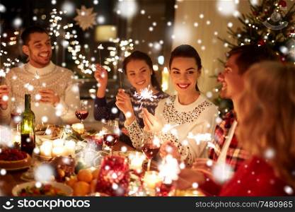winter holidays and people concept - happy friends with sparklers celebrating christmas at home feast over snow. happy friends celebrating christmas at home feast
