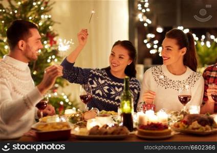 winter holidays and people concept - happy friends with sparklers celebrating christmas at home feast. happy friends celebrating christmas at home feast