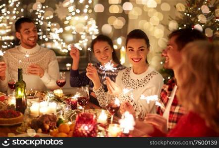 winter holidays and people concept - happy friends with sparklers celebrating christmas at home feast. happy friends celebrating christmas at home feast