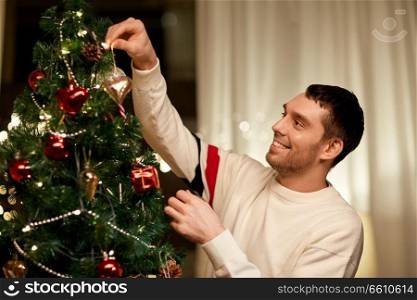winter holidays and people concept - happy man decorating christmas tree at home. happy man decorating christmas tree at home
