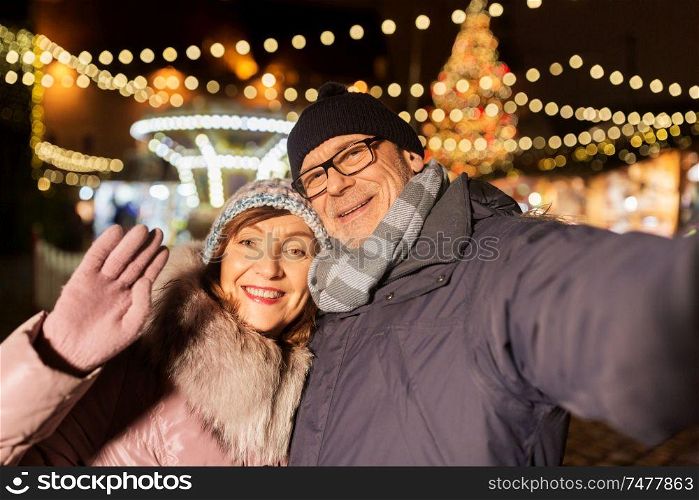 winter holidays and people concept - happy senior couple taking selfie at christmas market on town hall square in tallinn, estonia. senior couple taking selfie at christmas market