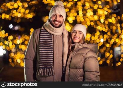 winter holidays and people concept - happy smiling couple hugging over christmas lights in evening. happy smiling couple hugging over christmas lights