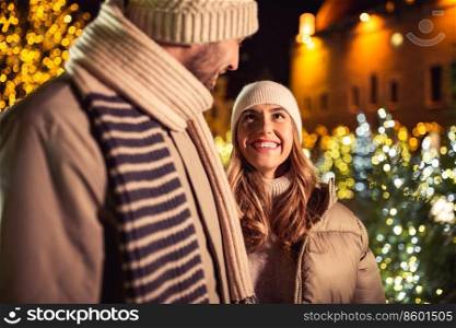 winter holidays and people concept - happy smiling couple over christmas tree lights in evening city. happy smiling couple over christmas lights