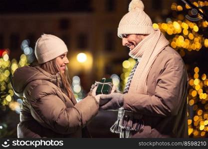 winter holidays and people concept - happy smiling couple with gift over christmas lights in evening. happy couple with gift over christmas lights