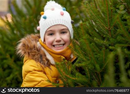winter holidays and people concept - happy smiling little girl choosing christmas tree at street market. little girl choosing christmas tree at market