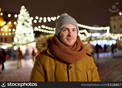 winter holidays and people concept - happy smiling man in hat, jacket and scarf at christmas market of tallinn town hall square. happy man in winter clothes at christmas market