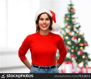 winter holidays and people concept - happy smiling young woman in santa helper hat over christmas tree lights background. happy young woman in santa hat on christmas