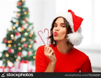 winter holidays and people concept - happy smiling young woman in santa helper hat with candy canes making duck face over christmas tree lights background. happy young woman in santa hat on christmas