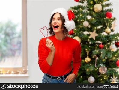 winter holidays and people concept - happy smiling young woman in santa helper hat with candy canes over christmas tree on background. happy young woman in santa hat on christmas