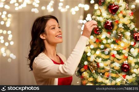 winter holidays and people concept - happy woman decorating christmas tree at home. happy woman decorating christmas tree at home