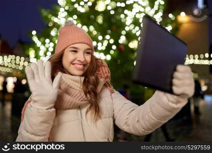 winter holidays and people concept - happy woman with tablet pc taking selfie or having video chat at christmas tree outdoors. woman with tablet pc at christmas tree outdoors