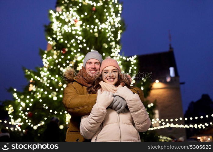 winter holidays and people concept - happy young couple dating and hugging at christmas tree in evening. happy couple hugging at christmas tree