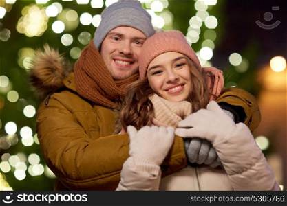 winter holidays and people concept - happy young couple dating and hugging at christmas tree in evening. happy couple hugging at christmas tree