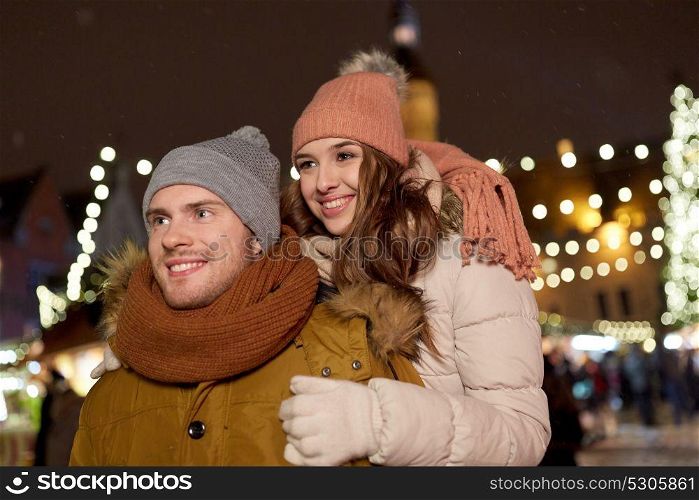 winter holidays and people concept - happy young couple dating and hugging at christmas market in evening. happy couple hugging at christmas market