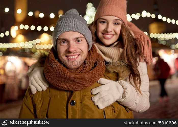 winter holidays and people concept - happy young couple dating and hugging at christmas market in evening. happy couple hugging at christmas tree