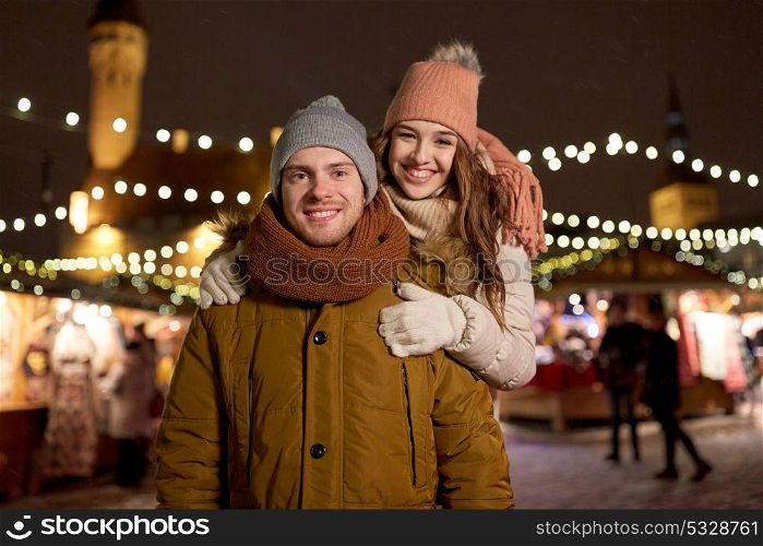 winter holidays and people concept - happy young couple dating and hugging at christmas market in evening. happy couple hugging at christmas market