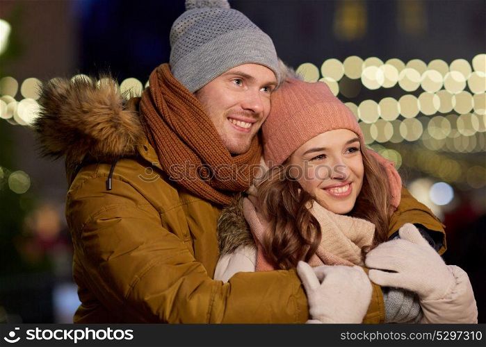 winter holidays and people concept - happy young couple dating and hugging in christmas evening outdoors. happy couple hugging at christmas tree