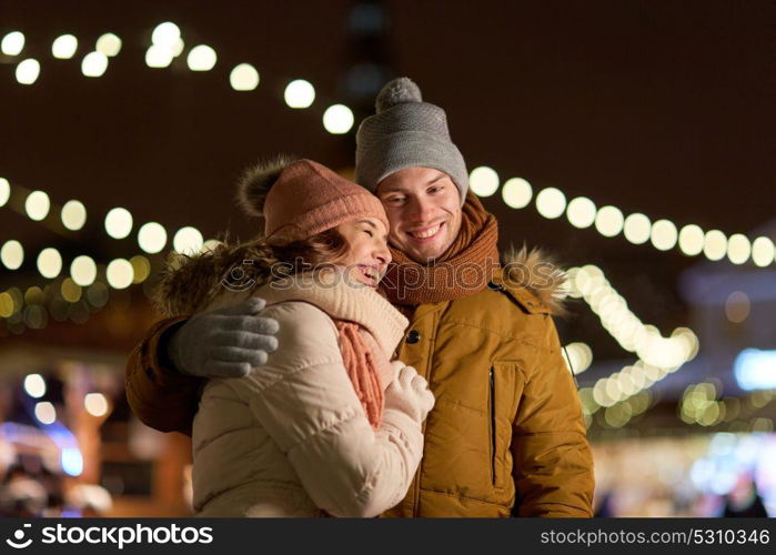 winter holidays and people concept - happy young couple dating and hugging in christmas evening outdoors. happy couple hugging at christmas tree