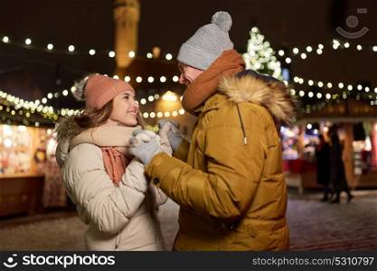 winter holidays and people concept - happy young couple dating at christmas market in evening. happy couple holding hands at christmas market