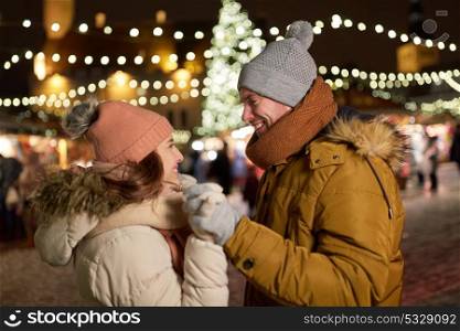 winter holidays and people concept - happy young couple dating at christmas market in evening. happy couple holding hands at christmas tree