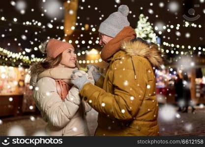 winter holidays and people concept - happy young couple dating at christmas market in evening. happy couple holding hands at christmas market