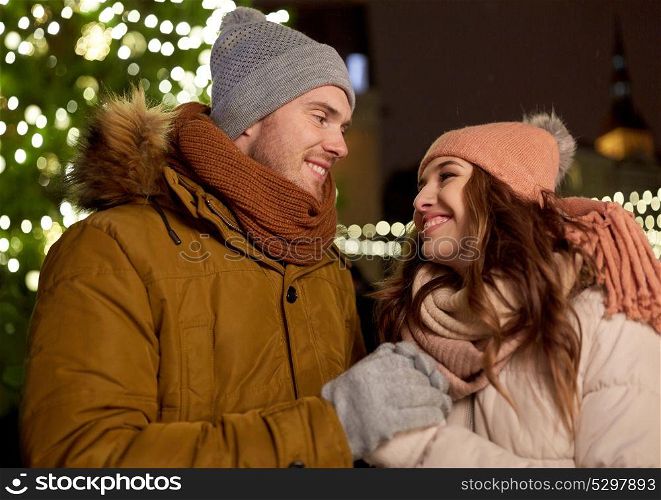 winter holidays and people concept - happy young couple dating at christmas tree in evening. happy couple holding hands at christmas tree