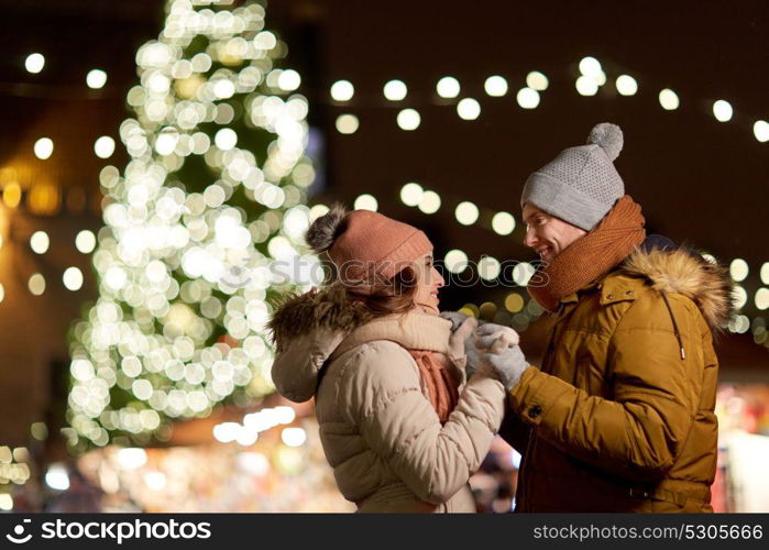 winter holidays and people concept - happy young couple dating at christmas tree in evening. happy couple holding hands at christmas tree