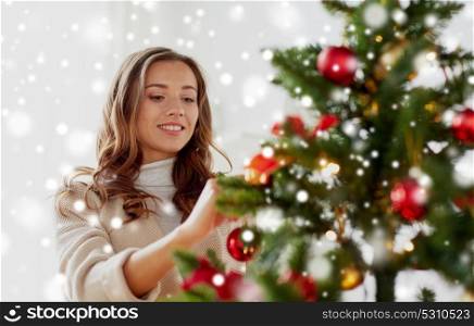winter holidays and people concept - happy young woman decorating christmas tree at home over snow. happy young woman decorating christmas tree