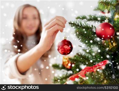 winter holidays and people concept - happy young woman decorating christmas tree over snow. happy young woman decorating christmas tree