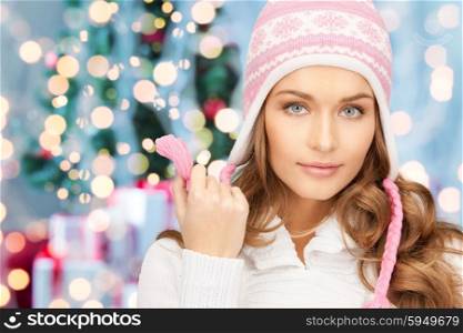 winter holidays and people concept - happy young woman in winter hat with over christmas tree lights background. happy woman in winter hat over christmas lights