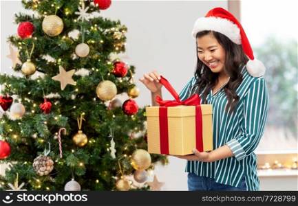 winter holidays and people concept - happy young woman opening gift box with red bow over christmas tree on background. happy woman opening christmas gift