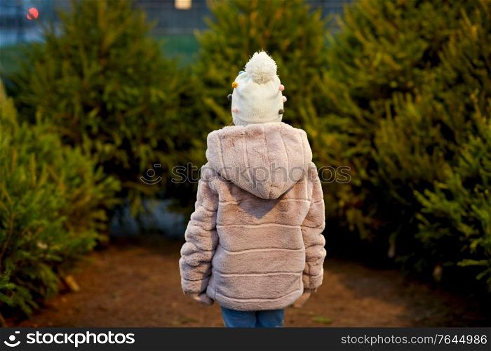 winter holidays and people concept - little girl choosing christmas tree at street market. little girl choosing christmas tree at market