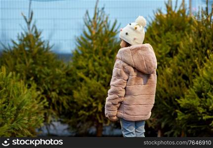 winter holidays and people concept - little girl choosing christmas tree at street market. little girl choosing christmas tree at market