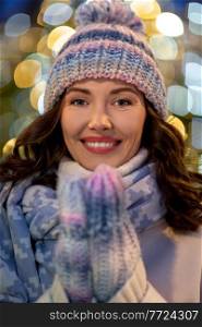 winter holidays and people concept - portrait of happy smiling young woman in hat, mittens and scarf over christmas lights. portrait of happy young woman in christmas lights