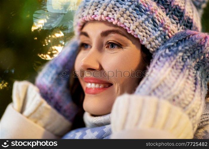 winter holidays and people concept - portrait of happy smiling young woman in hat, mittens and scarf over christmas lights. portrait of happy young woman in christmas lights