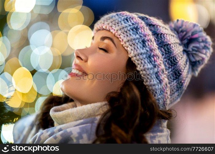 winter holidays and people concept - portrait of happy smiling young woman with closed eyes over christmas lights. portrait of happy young woman in christmas lights