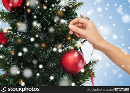 winter holidays, celebration and people concept - close up of hand decorating christmas tree with ball over blue background with snow
