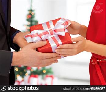 winter, holidays, celebration and people concept - close up of man and woman with present over living room with christmas tree background