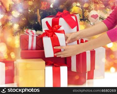 winter holidays, celebration and people concept - close up of woman putting present under christmas tree over lights