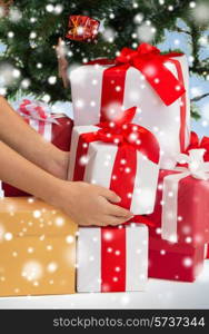 winter holidays, celebration and people concept - close up of woman putting present under christmas tree over blue background with snow