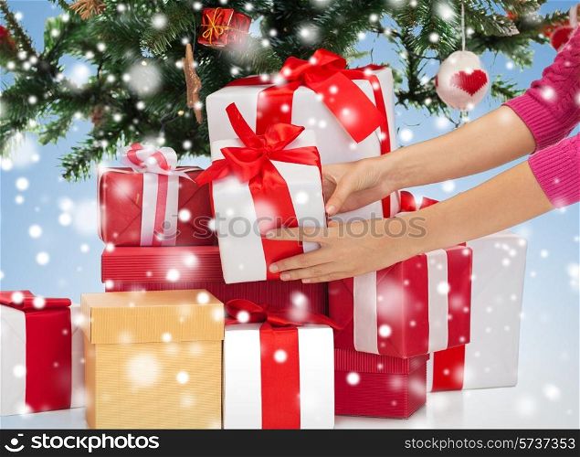 winter holidays, celebration and people concept - close up of woman putting present under christmas tree over blue background with snow