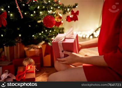 winter holidays, celebration and people concept - close up of woman with gift box at christmas tree at home. close up of woman with gift box at christmas tree
