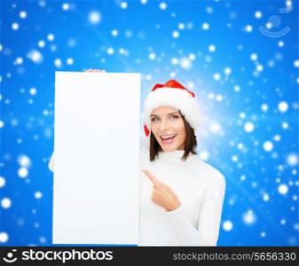 winter holidays, christmas, advertising and people concept - smiling young woman in santa helper hat with white blank billboard over blue snowing background